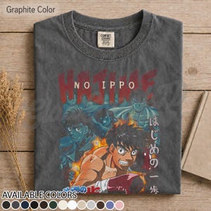 Op de afbeelding: Een grafietkleurig t-shirt met ronde hals en een grafische print van de anime Hajime No Ippo. Het ontwerp toont meerdere personages in een boksthema met rode tekst Hajime No Ippo en Japanse karakters aan de rechterkant van de print.