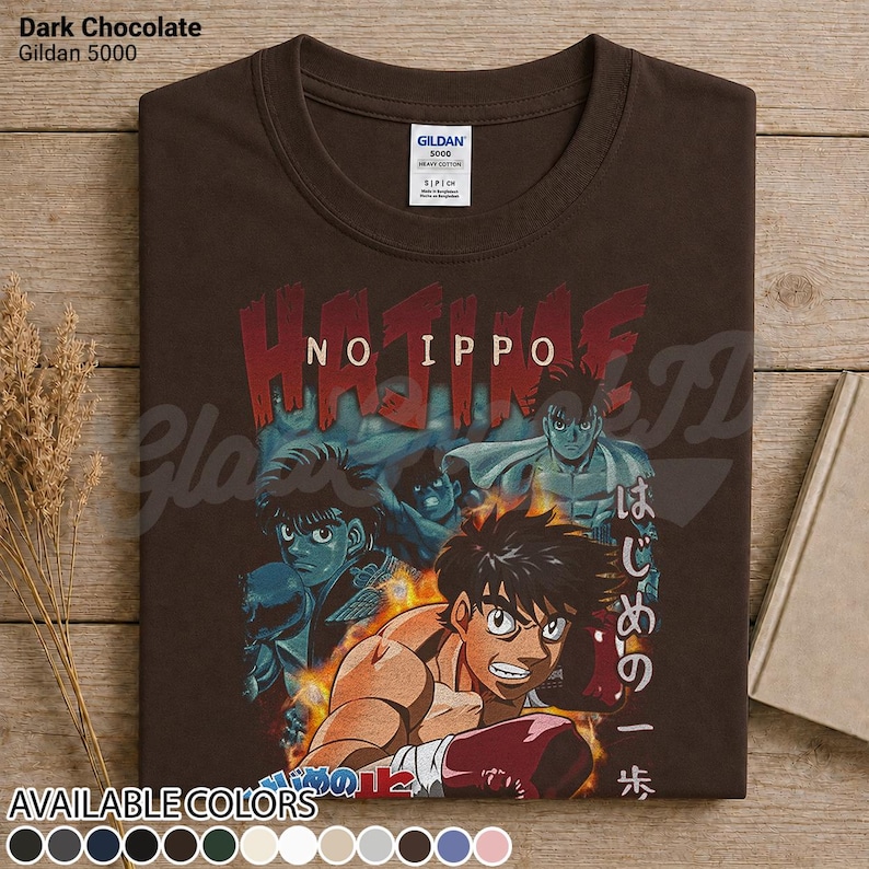 Op de afbeelding: Een donker chocoladebruin T-shirt met korte mouwen en een grafische print van de anime Hajime No Ippo. Het ontwerp toont meerdere personages in bokshoudingen, vlammen, de tekst Hajime No Ippo in het rood en Japanse tekens in het wit.