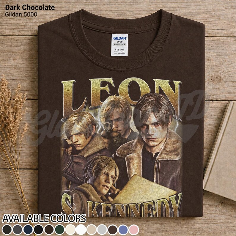 May include: A dark chocolate brown Gildan 5000 t-shirt featuring a graphic print of Leon Kennedy from Resident Evil. The design includes the name LEON KENNEDY in gold lettering and three depictions of the character wearing a brown jacket.