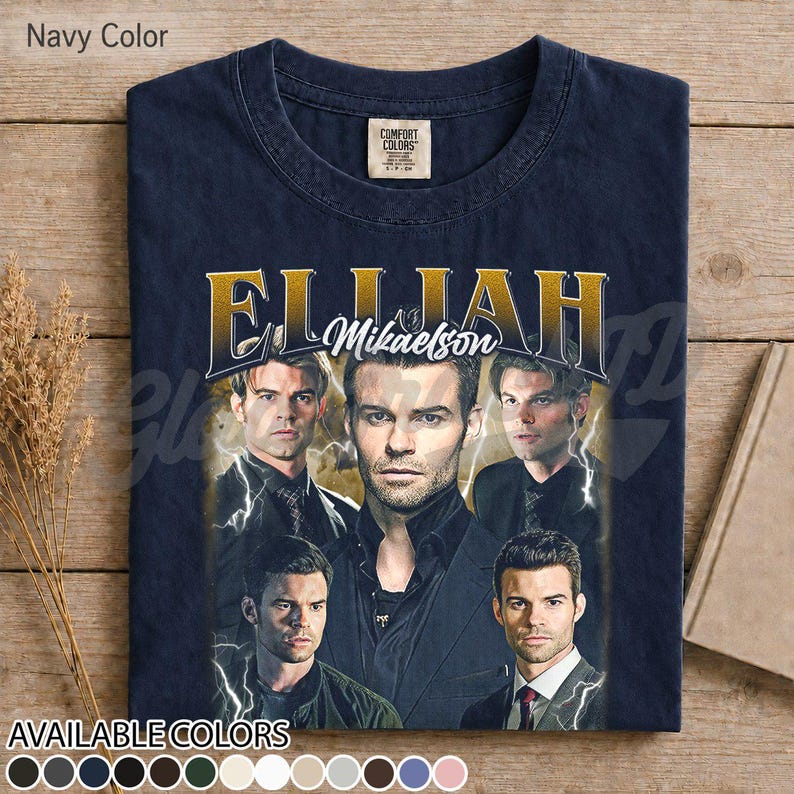 May include: Navy blue t-shirt with a graphic of Elijah Mikaelson and gold text reading "Elijah Mikaelson". The shirt has a vintage appearance and displays a range of available colours at the bottom.