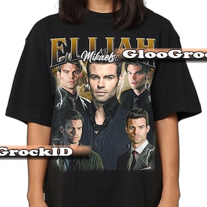 May include: Black t-shirt with a collage of images of a man and the text "Elijah Mikaelson" in gold lettering. The design includes lightning bolt graphics and a vintage aesthetic.