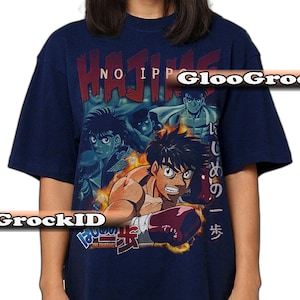 Op de afbeelding: Een marineblauw t-shirt met korte mouwen en een grafische print van personages uit de anime Hajime no Ippo. Het ontwerp bevat de tekst "HAJIME NO IPPO" in het rood, Japanse karakters en een centrale illustratie van een bokser met rode handschoenen.