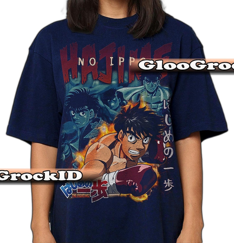 Op de afbeelding: Een marineblauw t-shirt met korte mouwen en een grafische print van personages uit de anime Hajime no Ippo. Het ontwerp bevat de tekst "HAJIME NO IPPO" in het rood, Japanse karakters en een centrale illustratie van een bokser met rode handschoenen.
