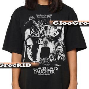 May include: Black t-shirt featuring a graphic from "The Blackcoat's Daughter" film. The design includes the film's title, a knife, and multiple faces. Text on the shirt reads "Abandoned as a child. Raised by the DARK."