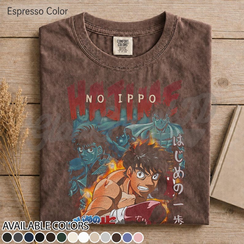 Op de afbeelding: Een espresso-kleurig t-shirt met korte mouwen en een grafische print van personages uit de anime Hajime No Ippo. Het ontwerp bevat de tekst Hajime No Ippo in het rood en Japanse karakters. Het shirt heeft een ronde hals en een Comfort Colors label.