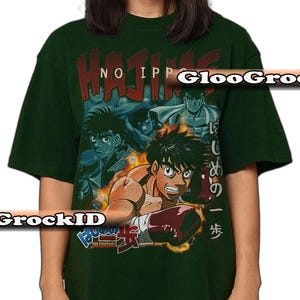 Op de afbeelding: Een donkergroen t-shirt met korte mouwen en een grafische print van anime-personages uit Hajime no Ippo. Het ontwerp bevat de tekst Hajime no Ippo in het rood en Japanse karakters, met een centrale figuur die rode bokshandschoenen draagt.