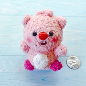 May include: Pink plush toy with a white belly and pink accents. The toy has a red nose and black eyes.