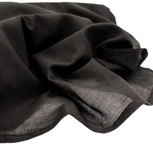 May include: A close-up of a black fabric, possibly a scarf or shawl, with soft folds and a slightly translucent appearance. The fabric is a solid black color and appears to be lightweight.