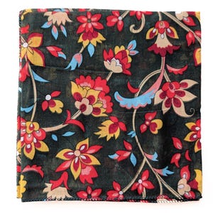 May include: A square, dark green scarf with a vibrant floral pattern. The design features red, yellow, and blue flowers with intricate details. The scarf is folded and appears to be made of a soft fabric.