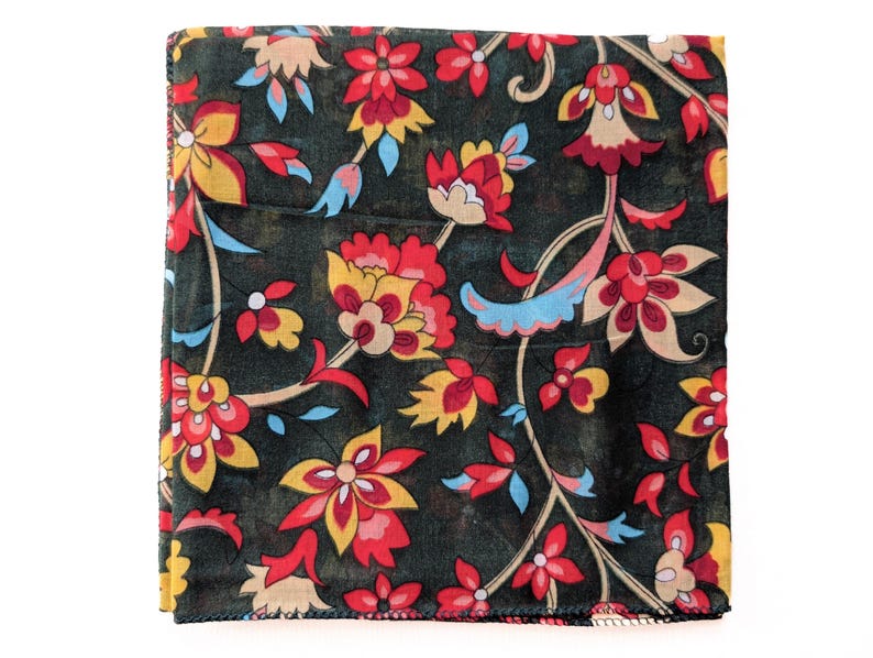 May include: A square, dark green scarf with a vibrant floral pattern. The design features red, yellow, and blue flowers with intricate details. The scarf is folded and appears to be made of a soft fabric.