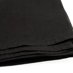 May include: Close-up of a stack of folded black fabric. The fabric appears to be linen or a similar material, with a slightly textured surface. The edges are neatly hemmed with a visible stitch.