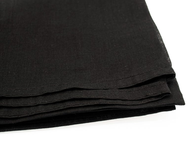 May include: Close-up of a stack of folded black fabric. The fabric appears to be linen or a similar material, with a slightly textured surface. The edges are neatly hemmed with a visible stitch.