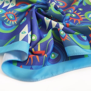 May include: A blue silk scarf with a colorful abstract pattern of eyes, circles, and geometric shapes. The scarf has a light blue border.