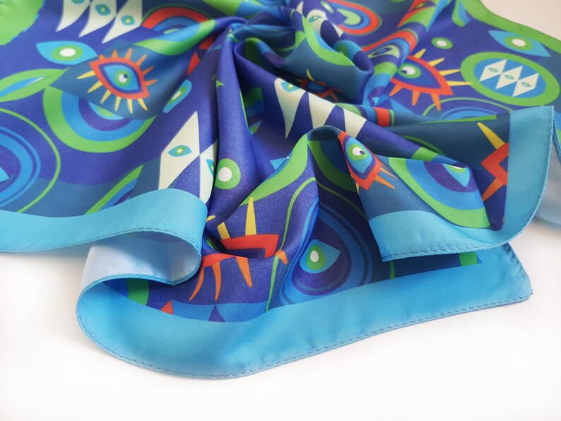 May include: A blue silk scarf with a colorful abstract pattern of eyes, circles, and geometric shapes. The scarf has a light blue border.
