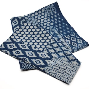 May include: A blue and white cotton fabric with a patchwork design featuring various geometric patterns. The fabric is folded in half and has a soft, textured feel.
