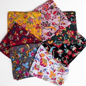 May include: An overhead shot displays a collection of colorful floral patterned bandanas. The bandanas are arranged in a starburst pattern, showcasing a variety of colors including yellow, burgundy, gray, black, and pink, each with intricate floral designs.