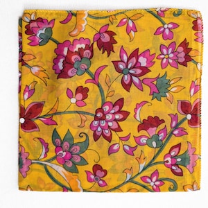 May include: A square, yellow fabric with a floral pattern. The design features pink, red, and green flowers with green leaves and stems. The fabric is folded and appears to be a scarf or handkerchief.