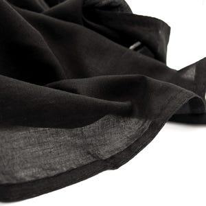 May include: Close-up of a flowing black fabric, possibly linen or a similar lightweight material. The fabric is draped and folded, with visible texture and shadows. The edges are neatly finished.