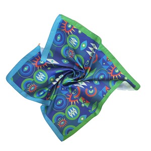 May include: A blue silk scarf with a green border and a colorful pattern of eyes and geometric shapes.