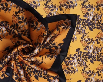 Könnte beinhalten: Ein gelber Seidenschal mit schwarzem Rand und einem schwarz-weißen Blumenmuster.