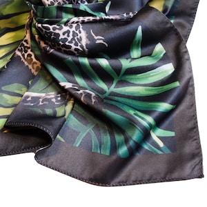 Op de afbeelding: Een donkergrijze zijden sjaal met een jungle-thema print. De sjaal heeft groene palmbladeren en een luipaardprint patroon. De randen zijn donkerder grijs, waardoor een rand rond het ontwerp ontstaat.