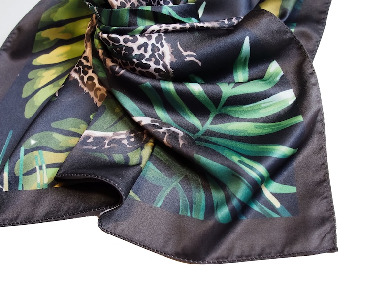Op de afbeelding: Een donkergrijze zijden sjaal met een jungle-thema print. De sjaal heeft groene palmbladeren en een luipaardprint patroon. De randen zijn donkerder grijs, waardoor een rand rond het ontwerp ontstaat.