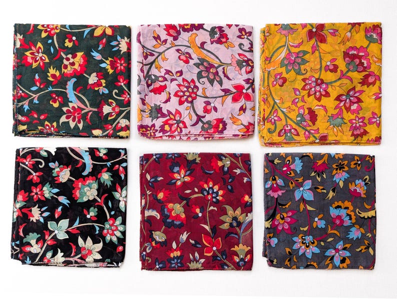 May include: Six folded square scarves with floral patterns. The scarves feature a variety of colors, including black, dark green, burgundy, yellow, and pink. Each scarf has a unique floral design with red, yellow, and blue accents.