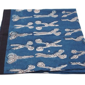 May include: A blue cotton fabric with a white and black pattern of scissors. The fabric has a dark blue border.