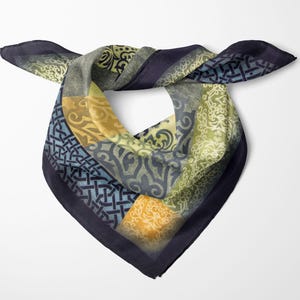 Op de afbeelding: Een vierkante sjaal met een donkerblauwe rand en een patchwork ontwerp. De sjaal heeft ingewikkelde patronen in tinten blauw, groen en goud. De sjaal is gevouwen en geknoopt, wat de verscheidenheid aan patronen en kleuren laat zien.