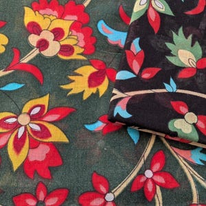 May include: Close-up of two pieces of fabric with a floral pattern. One piece is dark green with red, yellow, and white flowers. The other piece is black with a similar floral design in red, green, and blue.