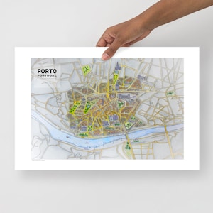 Peut inclure: Une carte détaillée de Porto, Portugal, avec le plan de la ville en tons or et gris. La carte comprend le texte "PORTO PORTUGAL" dans le coin supérieur gauche. La carte est tenue par une main.