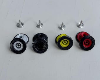 以下が含まれることがあります： カラフルなジーンズボタンとリベットのコレクション。ボタンは黒い縁に白、黄色、赤の中心があります。リベットはシルバーです。ボタンには「USA JEANS」と表示されています。