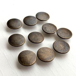 May include: Ten round, flat, brass-coloured buttons with a slightly textured surface.