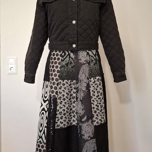 Könnte beinhalten: Eine schwarze, gesteppte Jacke mit Kragen und silbernen Knöpfen kombiniert mit einem wadenlangen Rock im Patchwork-Design aus verschiedenen schwarzen, weißen und grauen Mustern, darunter Punkte, Leopardenmuster und abstrakte florale Motive.