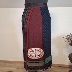Peut inclure: Un haut à col roulé gris et une longue jupe sur un mannequin. La jupe présente un motif patchwork avec des panneaux rouges, bleus et à motifs, et un détail ovale brodé. La jupe a un ourlet à franges.