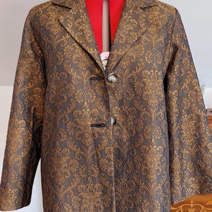 Könnte beinhalten: Ein gold- und braunes gemustertes Blazer mit schwarzem Knopfverschluss. Der Blazer befindet sich auf einem Mannequin und hat ein rotes Futter.