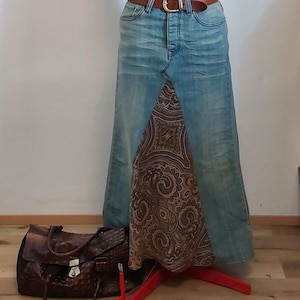 Könnte beinhalten: Ein langer Jeansrock mit einem braunen Paisley-Muster-Einsatz. Der Rock wird mit einem braunen Ledergürtel mit goldener Schnalle getragen. Eine braune Lederhandtasche liegt auf dem Boden.