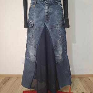 Può includere: Gonna di jeans patchwork con pannello centrale blu scuro. La gonna ha tasche ed è esposta su un supporto rosso. La modella indossa una maglia grigia a maniche lunghe. Il design della gonna incorpora vari pezzi di denim.