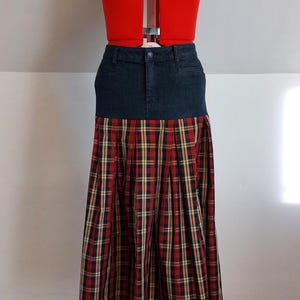 Könnte beinhalten: Eine rote Schneiderpuppe mit einem Jeansrock und einem plissierten karierten Rock. Der karierte Rock hat ein rotes, schwarzes und gelbes Muster. Die Schneiderpuppe steht auf einem roten Ständer.