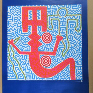 Peut inclure: Une affiche rectangulaire présentant un fond bleu vif avec un graphique carré central. Le graphique affiche des personnages stylisés orange et verts soulignés de noir, entourés d'un motif dense de symboles géométriques bleus et blancs.