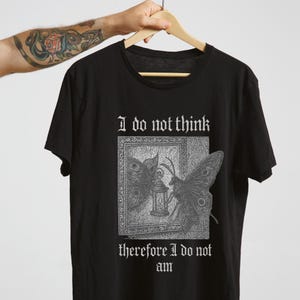 Puede incluir: Camiseta negra con un diseño gótico de mariposas y una linterna. El texto "I do not think, therefore I do not am" está impreso encima y debajo del diseño en una fuente gótica.