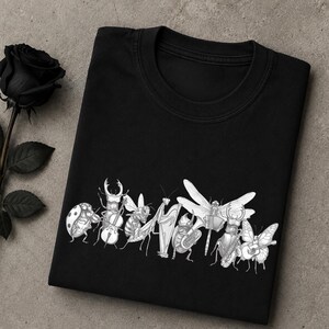 Może przedstawiać: Czarny t-shirt z białą grafiką przedstawiającą różne owady grające na instrumentach muzycznych, w tym biedronkę, jelonka rogacza z wiolonczelą, pszczołę z fletem, modliszkę z harfą oraz motyla z gitarą, tworzące wspólnie orkiestrę owadów.