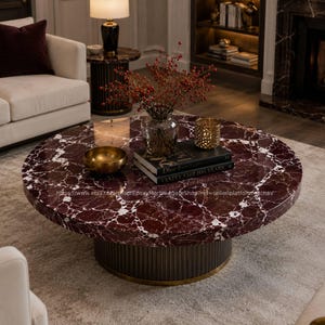 May include: A round coffee table with a burgundy marble top and white veining. The table has a dark brown base with a gold trim. A gold bowl, books, and a vase with red berries are on the table.