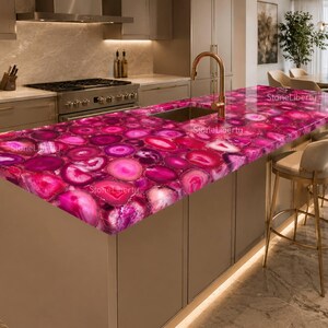 May include: A kitchen island countertop featuring a vibrant pink agate gemstone surface with a polished finish. The slab displays natural concentric banding patterns in various shades of magenta and fuchsia, integrated with a gold faucet and sink.
