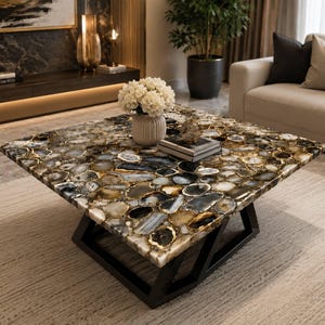 May include: A square coffee table featuring a tabletop constructed from a mosaic of polished, multi-colored agate slices in shades of gray, brown, and white. The table is supported by a black, angular metal base with a geometric frame design.