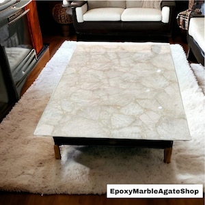 May include: A white coffee table with a clear epoxy resin top featuring a natural agate pattern. The table is on a white shag rug. The text "EpoxyMarbleAgateShop" is visible in the lower right corner of the image.