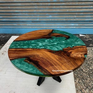 Può includere: Un tavolino rotondo con piano in legno e centro in resina epossidica turchese. Il legno presenta un motivo a venature naturali e il tavolo è sostenuto da tre gambe nere. Il testo "EpoxyMarbleAgateShop" è visibile.