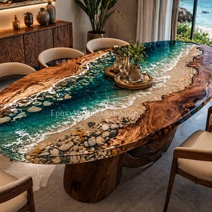 Op de afbeelding: Een ovale eettafel met een strandthema-ontwerp. De tafel heeft een houten voet en een blad dat een kustlijn nabootst met blauwe hars die de oceaan, zand en kiezels voorstelt. De tafel is omringd door beige stoelen.