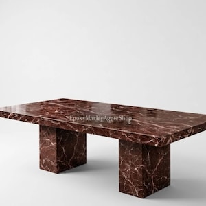 May include: A rectangular marble table with a rich burgundy color and white veining. The table has a solid, block-like base and a polished surface. The table is a statement piece for any living space.