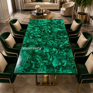 Può includere: Un tavolo da pranzo rettangolare con una superficie dal motivo malachite verde brillante e una base in metallo dorato, circondato da sei poltrone in velluto verde scuro con finiture dorate e cuscini beige. Il testo StoneLiberty è visibile.